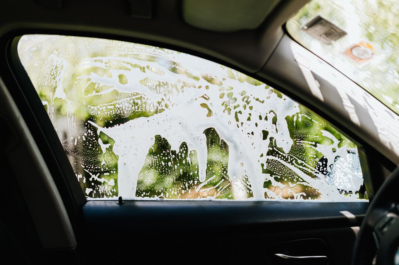 services-01 View from inside a car showing soapy water on the window during a car wash.